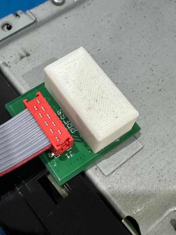 Bezinwazyjny adapter JTAG (jig) serwisu OEMatic podłączony do płyty głównej (PCB) radia Nissan LCN podczas odblokowywania.