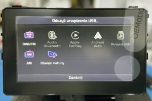 Ekran radia Kia Sportage z komunikatem Odczyt urządzenia USB i ikonami źródeł audio DAB FM Bluetooth CarPlay Android