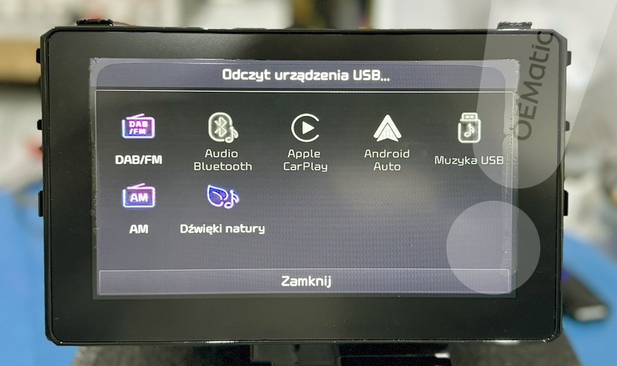 Ekran radia Kia Sportage z komunikatem Odczyt urządzenia USB i ikonami źródeł audio DAB FM Bluetooth CarPlay Android Auto